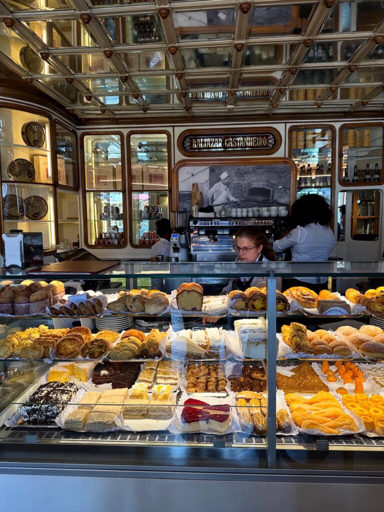 7 Best Pastel de Nata in Lisbon (I've Tried Them All Now) 9 Buttery pastries and cakes displayed in a glass case at a traditional Portuguese bakery in Lisbon, showcasing authentic local desserts and baked goods in a charming setting.