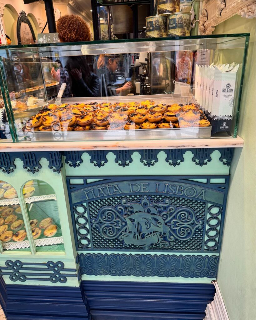 7 Best Pastel de Nata in Lisbon (I've Tried Them All Now) 8 Crispy pastel de nata pastries in display case at Lisbon bakery, traditional Portuguese dessert, LisbonVibes, decorated vintage-style bakery, authentic Lisbon sweets, Portuguese pastry shop, iconic Lisboa treats, Lisbon culinary experience.