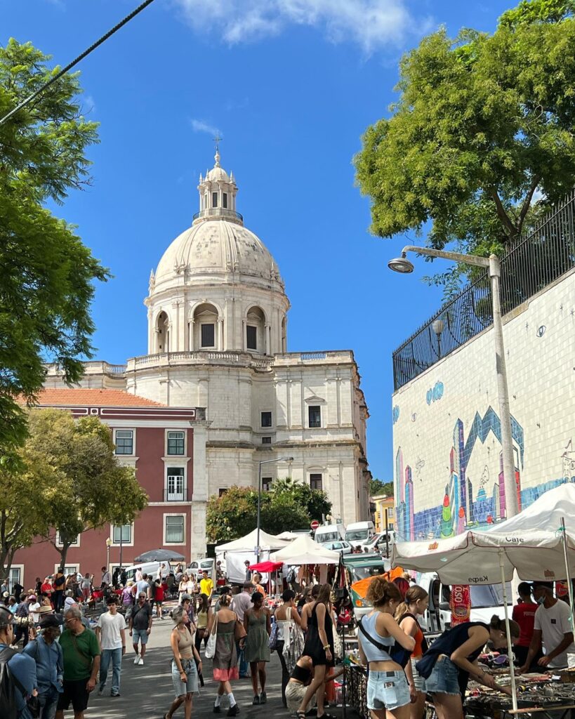 Alfama in Lisbon: A Tourist Guide 14 Alfama in Lisbon, Portugal, bustling with tourists exploring historic streets, local markets, and vibrant cafes under a clear blue sky.