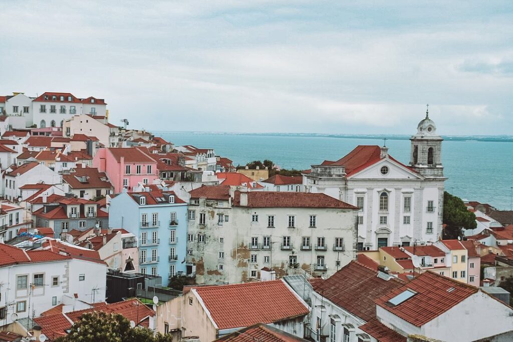 Alfama in Lisbon: A Tourist Guide 3 Alfama district in Lisbon with colorful historic buildings, narrow streets, and the Tagus River in the background, showcasing the charm and vibrant atmosphere of this iconic neighborhood.
