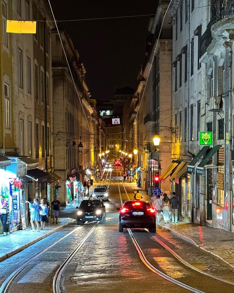 Alfama in Lisbon: A Tourist Guide 7 Night view of Alfama district in Lisbon with tram tracks, illuminated shops, and pedestrians enjoying the vibrant atmosphere.