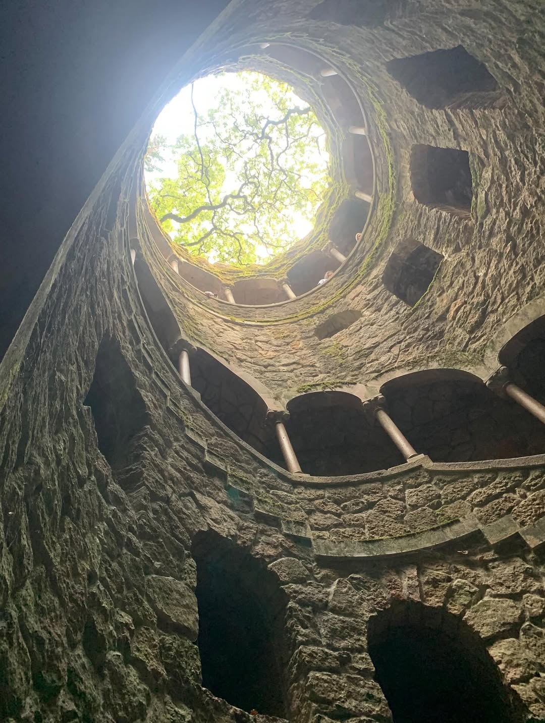 21 Amazing Castles in Lisbon and Its Surroundings 9 Ancient stone well in Lisbon with a view of the sky and a tree canopy at the top.