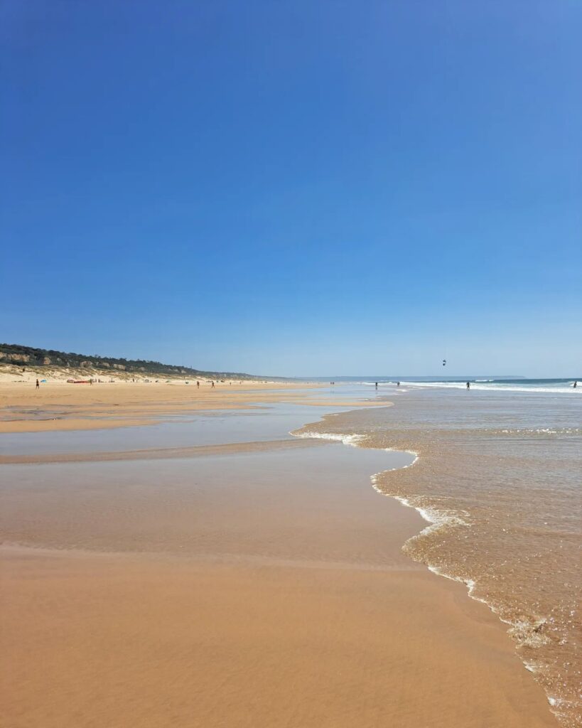 Scenic view of Lisbon's best beaches featuring golden sands, gentle waves, and a bright blue sky, perfect for sunbathing, swimming, and seaside activities.