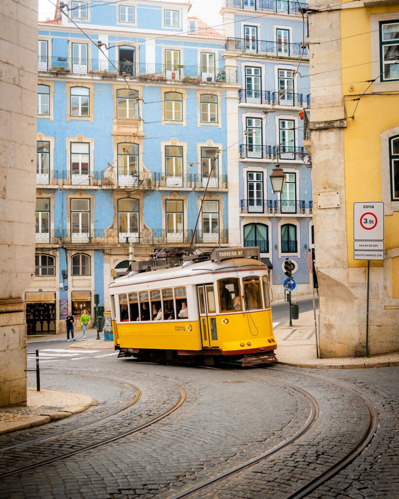 Alfama in Lisbon: A Tourist Guide 20 Vintage yellow tram navigating through Alfama district in Lisbon, Portugal, with vibrant pastel buildings and cobblestone streets.