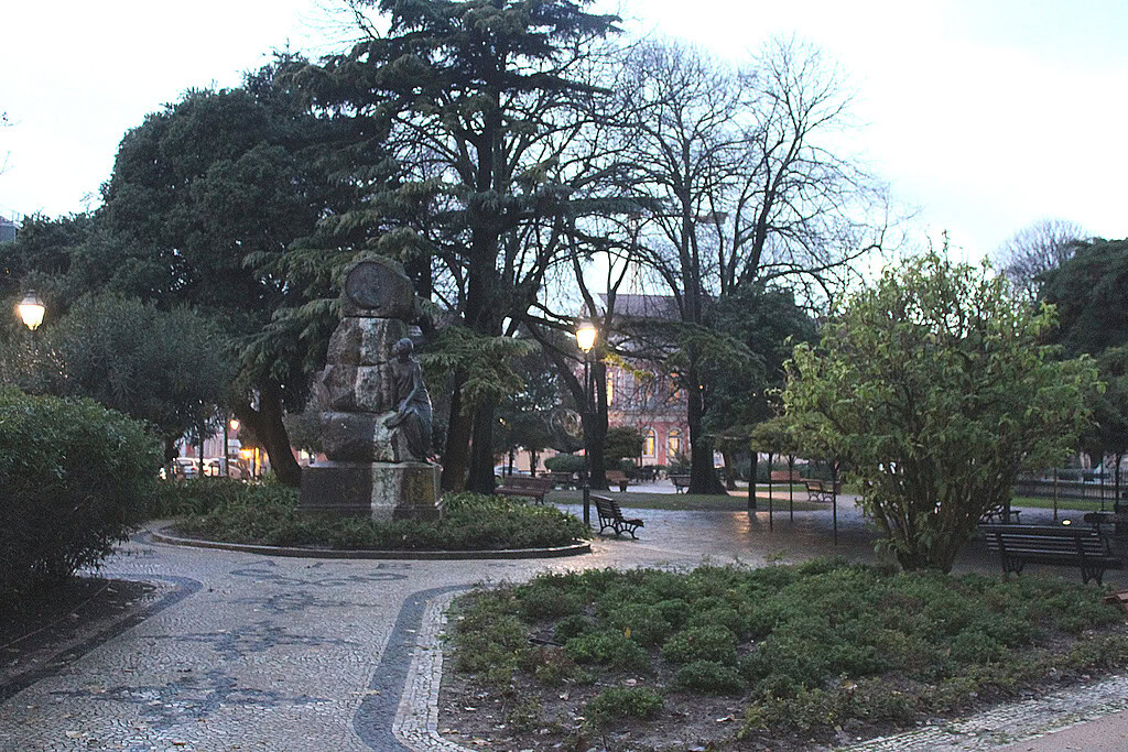 Principe Real: What to Do, Stay, Eat, and More 1 Scenic view of Principe Real Park in Lisbon with trees, pathways, and a statue during early evening.