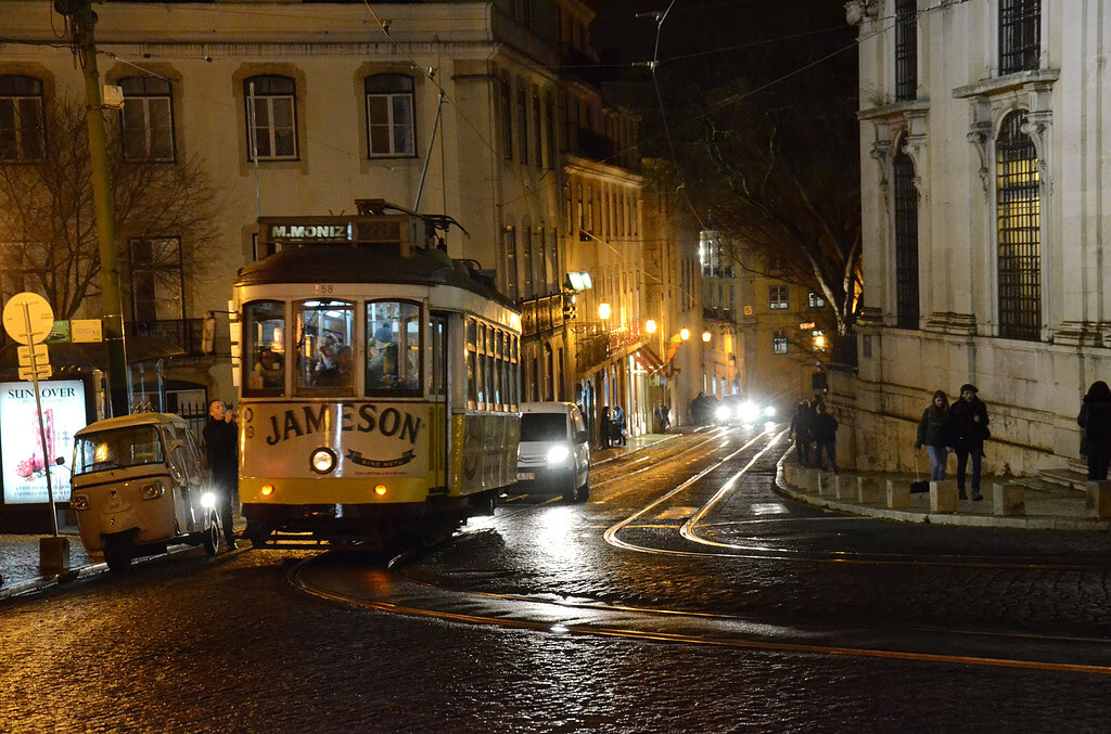 23 Things to Do in Lisbon at Night 1 Historic Lisbon tram at night on wet cobblestone streets with city lights illuminating the scene.