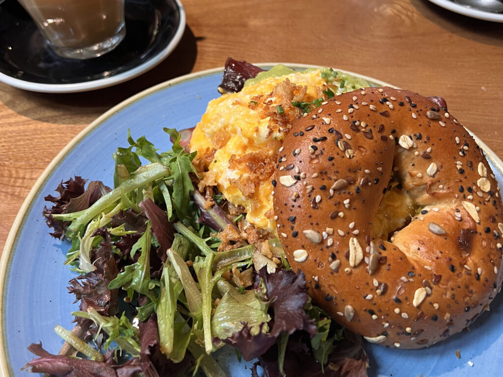 Lisbon Food Guide: What to Eat + Where to Eat (Local Tips + Map) 4 Freshly prepared breakfast with scrambled eggs, assorted greens salad, and a seeded bagel, served at a cozy Lisbon café, showcasing the vibrant local food scene and inviting atmosphere for a memorable Lisbon dining experience.