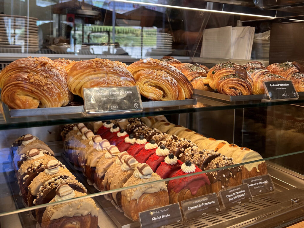 Lisbon Food Guide: What to Eat + Where to Eat (Local Tips + Map) 5 Soft and flaky Portuguese pastries, including croissants and éclairs, displayed in a bakery window with a cozy ambiance, perfect for enjoying authentic Lisbon sweets and desserts.