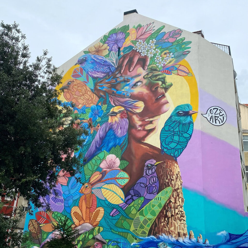 Graça Lisbon: A Neighborhood Guide 10 Colorful mural depicting a woman with a floral headdress and birds in Graça neighborhood, Lisbon, showcasing urban art and local culture.